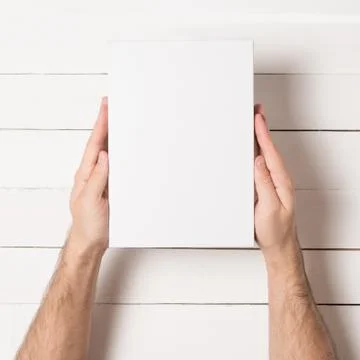 White rectangular box in male hands. Top view. White table on the background 写真素材
