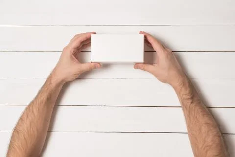White rectangular box in male hands. Top view. White table on the background 스톡 사진