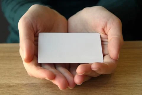 A white rectangular card lies in the opened palms of a girl in a blue sweater Stockfoto's