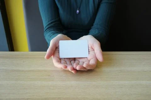A white rectangular card lies in the opened palms of a girl in a blue sweater 写真素材