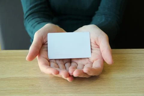 A white rectangular card lies in the opened palms of a girl in a blue sweater Stock Photos