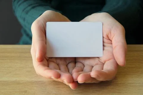 A white rectangular card lies in the opened palms of a girl in a blue sweater 스톡 사진