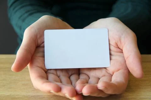 A white rectangular card lies in the opened palms of a girl in a blue sweater Stock Photos