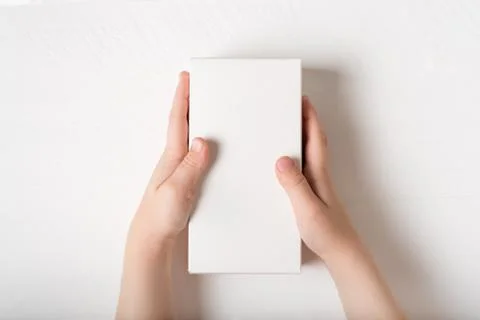 White rectangular cardboard box in children's hands. Top view, white backgrou 스톡 사진