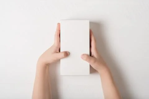 White rectangular cardboard box in children's hands. Top view, white backgrou Stock Photos