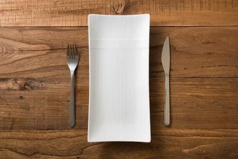 White rectangular Plate with fork and knife on brown wooden background Stock Photos