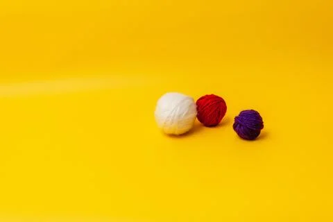 White, red and blue balls of wool lie on a yellow background Stock Photos