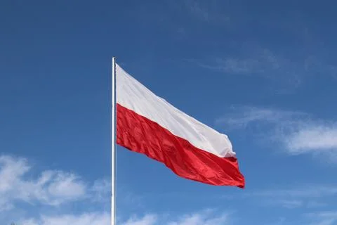 White-red horizontal flag on a flagpole developing in the wind against a blue Stock Photos