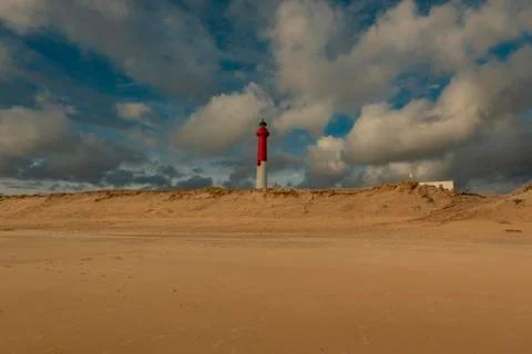 White red lighthouse with clouds at the sandy beach behind the dune Stock Photos