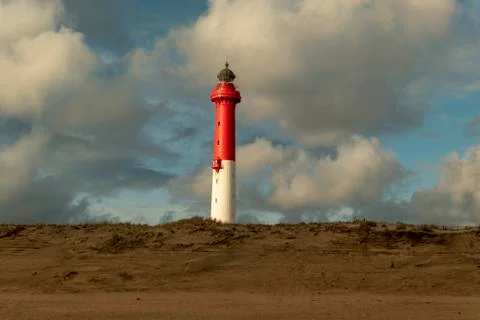 White red lighthouse with clouds at the sandy beach behind the dune Stock Photos