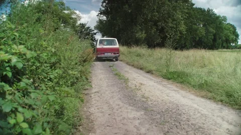 White red retro T3 van driving away on rural dirt road, behind shot Stock Footage 161935362