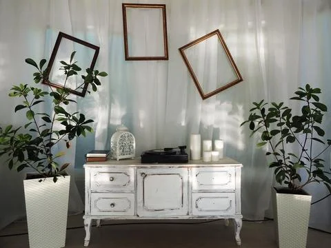 A white retro commode with a record player, empty frames on white drapery, and Stock Photos