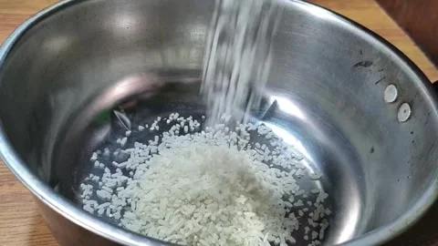 White rice grains falling into a stainless steel cooking pot on a wooden table. Stock Footage 330517247