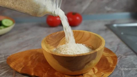 White rice is poured out of a kitchen glass jar into a deep wooden bowl 스톡 동영상 304748219