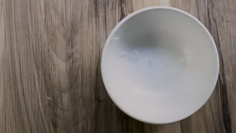 White rice starting to fall into white bowl on wooden table, copy space 4K Stock Footage 342431344