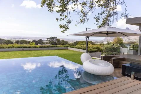 White ring lounge floating on infinity pool ledge under umbrella by wooden deck, Foto stock
