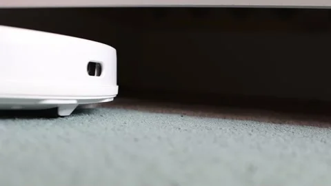 A white robot vacuum cleaner cleans the carpet and drives Stock Footage 166036071