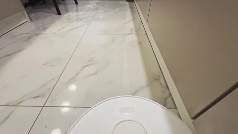 A white robot vacuum cleaner is on the floor next to a toilet 库存影片 278443320