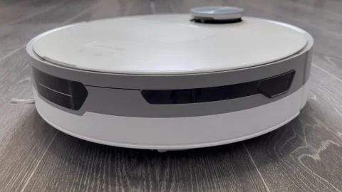 White robot vacuum cleaner moves from left to right on gray laminate flooring Stock Footage 305053357
