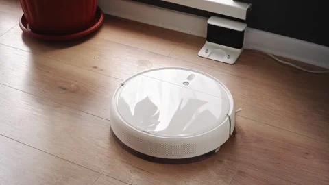 White robot vacuum cleaner returning to charging station on wooden floor Stock Footage 303353644