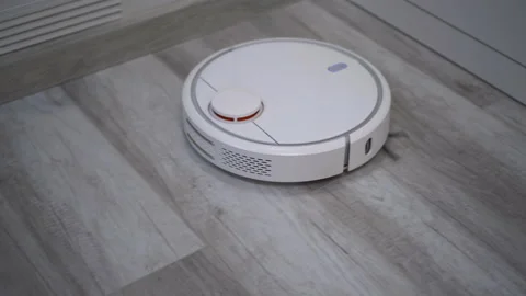 A white robot vacuum cleaner rides on a white parquet floor. The robot with Video stock 171940539