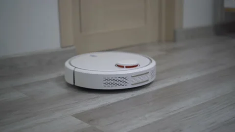 A white robot vacuum cleaner rides on a white parquet floor. The robot with Video stock 171940561
