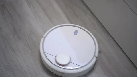 A white robot vacuum cleaner rides on a white parquet floor. The robot with 库存影片 171940624