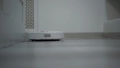 A white robot vacuum cleaner rides on a white parquet floor. The robot with Stock Footage 171940663