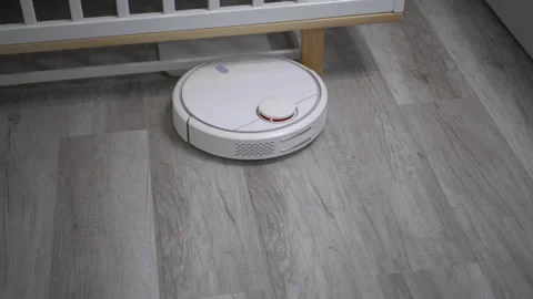 A white robot vacuum cleaner rides on a white parquet floor. The robot with Stock Footage 171940892