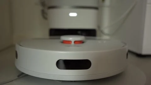 A white robot vacuum cleaner is sitting on a white surface Stock-Footage 274968245