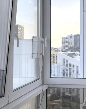 White robot window cleaner attached to a PVC window with urban cityscape vi.. 스톡 사진