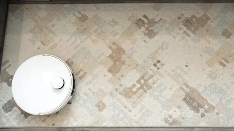 White robotic vacuum cleaner operates across patterned carpet surface Stock Footage 345023943