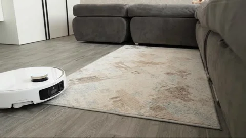 White robotic vacuum cleaner operates across patterned carpet surface Stock Footage 345023959