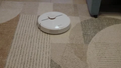 White robotic vacuum moving across patterned beige carpet Stock Footage 342863980