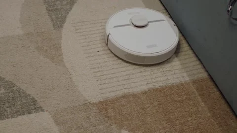 White robotic vacuum navigating patterned carpet Stock Footage 342864238