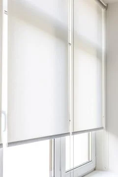 White roller blinds covering a window in a modern room during daylight hours Stock Photos