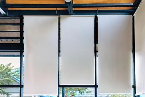 White roller blinds installed on large windows of modern room. .Inside view.. Stock Photos