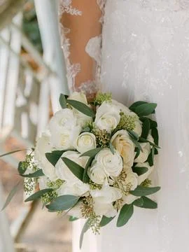 White rose bouquet held by a bride wearing a lace wedding dress outdoors in a Stock Photos