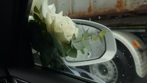 White rose bouquet reflected in car side mirror with raindrops and wet roadside Stock Footage 345530359