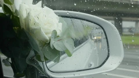 White rose bouquet seen through rain covered car window with side mirror and Stock Footage 345530516