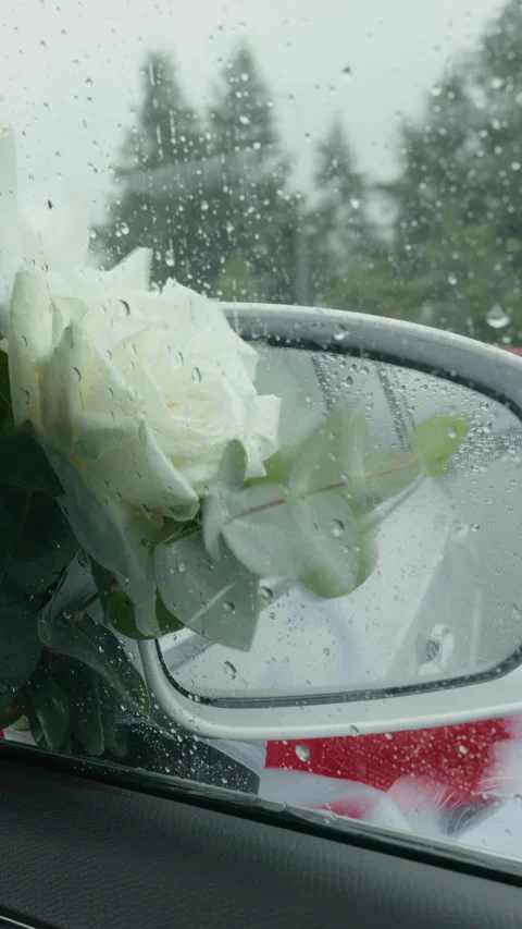 White rose bouquet seen through rain covered car window beside side mirror Stock Footage 345531543