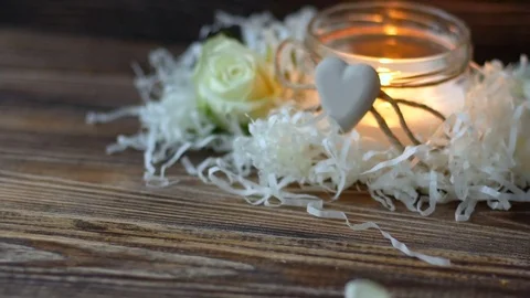 White rose petals falling on dark table, burning candle on background Video stock 77319215