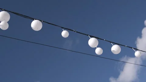 White round lanterns strung along a black wire against a bright blue sky with Stock Footage 336623130