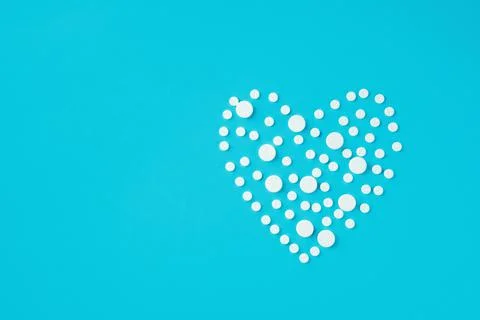 White round pills of different size in shape of heart on blue background Stock Photos