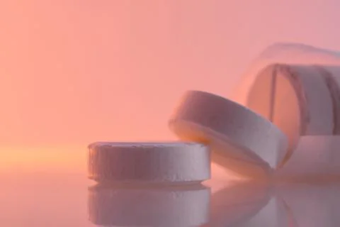 White round pills on a mirror surface, closeup. Medicines on glass lit by the 库存照片