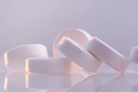 White round pills on a mirror surface, closeup. Medicines on glass lit by the Stock Photos