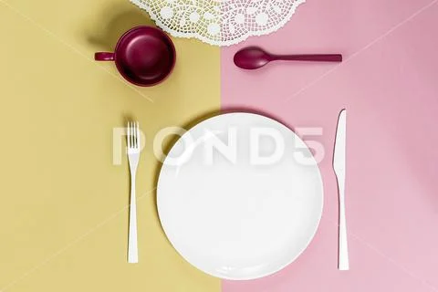 White round plate and cutlery on a light pink-green background.. Stock Photos