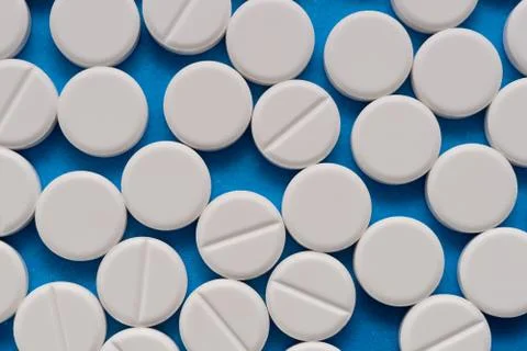 White round tablets on a blue background. Macro of white capsules on blue bac Stock Photos
