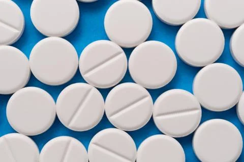 White round tablets on a blue background. Macro of white capsules on blue bac Stock Photos