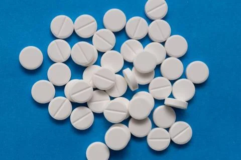 White round tablets on a blue background. Macro of white capsules on blue bac Stock Photos